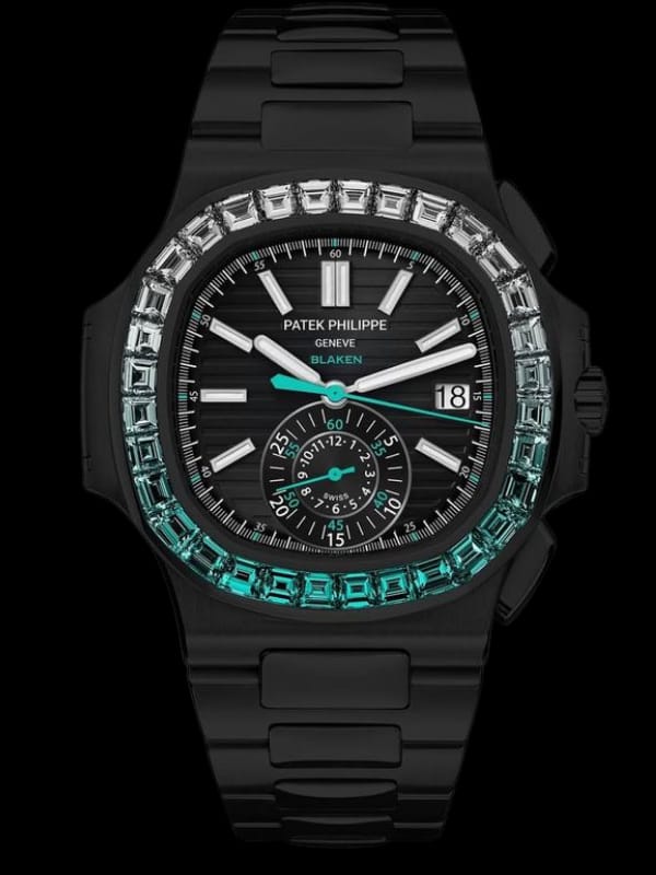 A luxury Patek Philippe watch with a black dial, emerald-accented bezel, and black strap, featuring detailed markers and a date window,